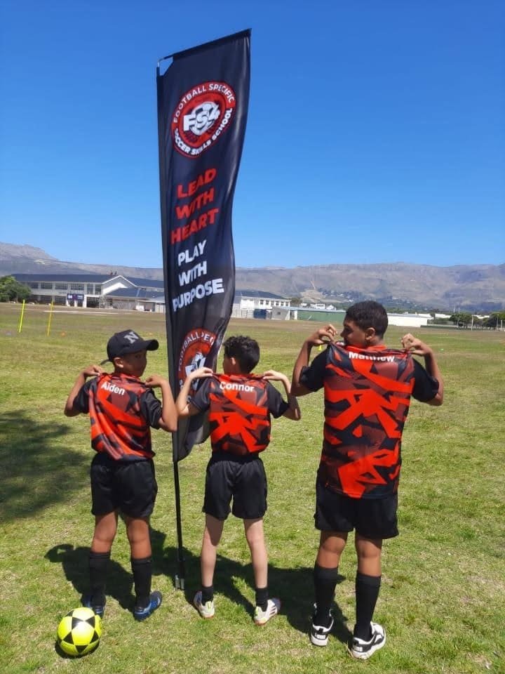 Three young FS4 players holding the FS4 team flag reading 'Lead With Heart, Play With Purpose'